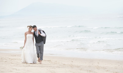 Wall Mural - Happy bride and groom walking on the beach