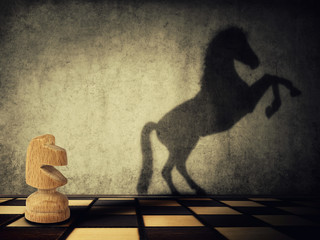 Magical transformation as a wooden knight chess piece casting a shadow of a wild horse on two legs on the wall. Symbol of business aspirations, freedom and leadership concept. 