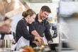 © Cavan Images - Male chef assisting coworker while cooking in the restaurant kitchen