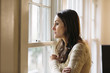 © Cavan Images - Side view of thoughtful woman standing by window at home