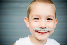 Close-up Portrait Of Happy Boy With Artificial Mustache Against Wall