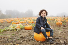 Portrait Of Boy Sitting On Pumpkin At Farm During Foggy Weather