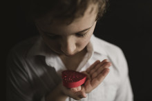 Close-up Of Boy Holding Red Heart Shape Object In Darkroom At Home