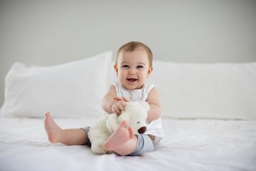 cute baby girl playing with soft toy on bed