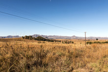 Winter Grassland With Overhead Power Lines Against Mountain Range