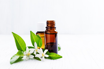 Neroli (Citrus aurantium) essential oil in a brown glass bottle with fresh white  flowers on ligth background. Selective focus.