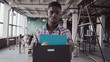 Young african man get fired from work at start-up. Male walks through the office, carrying box with personal belongings.