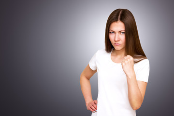 Closeup portrait of young angry annoyed woman with bad attitude giving talk to hand gesture showing fist. isolated grey wall background. Negative human emotion facial expression feeling body language