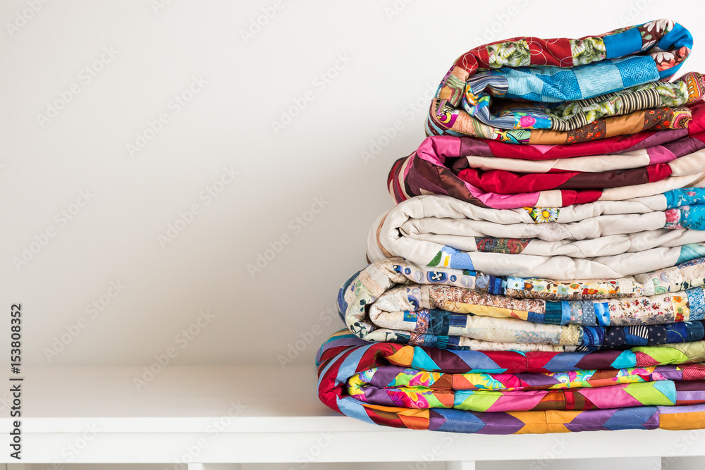 sewing and fashion concept - stack of colorful quilts, beautiful bedspreads stacked in several rows in height for storage, sale patchwork productions on a white background, copy space - obrazy, fototapety, plakaty 