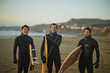 © Erickson Stock - Portrait of smiling friends holding surfboard on beach