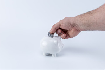 Caucasian hand holding a coin and putting depositing on a piggy saving bank moneybox