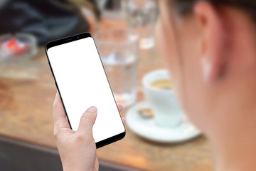Poster - Woman holding modern smart phone with isolated screen for mockup. View behind shoulder. Desk with coffee in background.