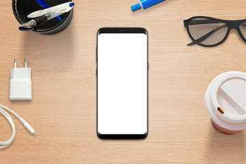 Poster - Modern mobile phone on table with isolated screen. Coffee, glasses, pens, charger beside.