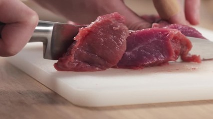 Wall Mural - Slow motion slide shot of young female hand cutting raw beef with a knife on plastic board, 180fps prores footage