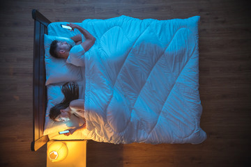The man and woman phone on the bed. evening night time. view from above