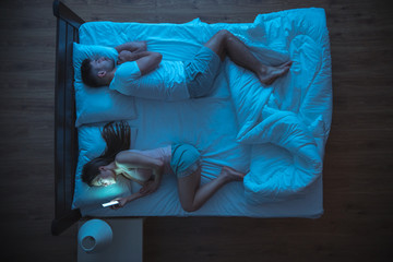 The woman with phone lay near husband. night time. view from above