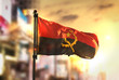 Angola Flag Against City Blurred Background At Sunrise Backlight