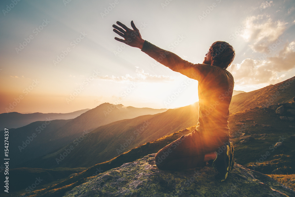 Man praying at sunset mountains raised hands Travel Lifestyle spiritual relaxation emotional concept vacations outdoor harmony with nature landscape - obrazy, fototapety, plakaty 