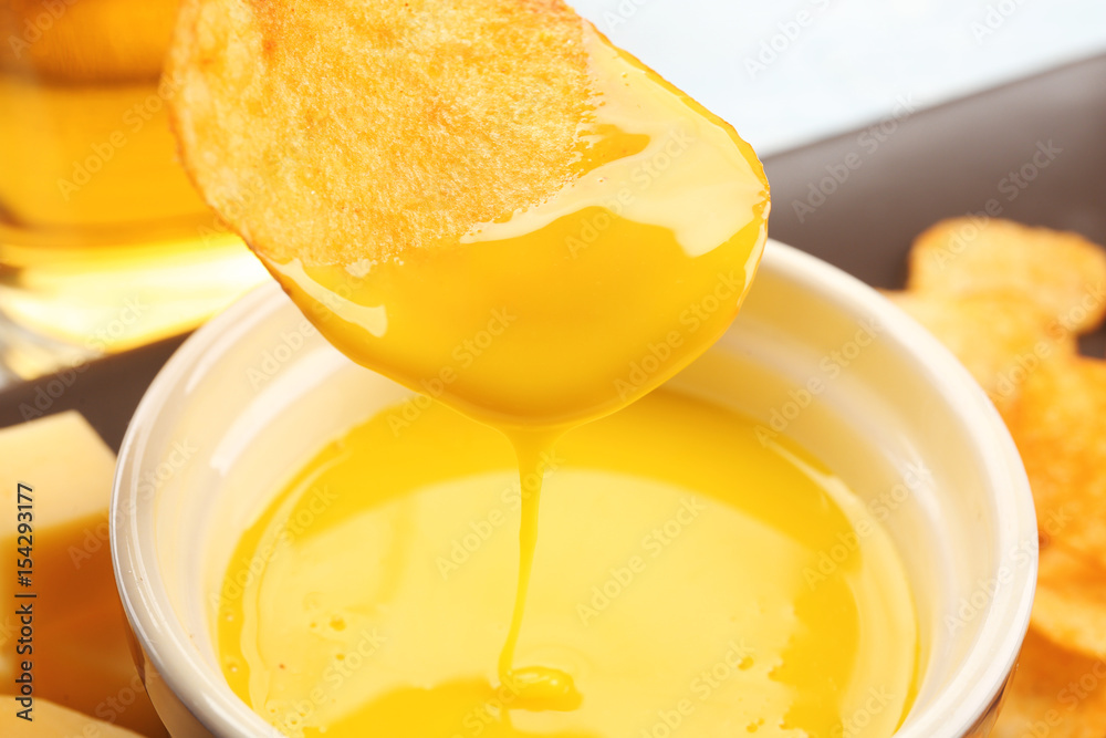 Dipping chips into bowl with creamy cheese sauce, close up