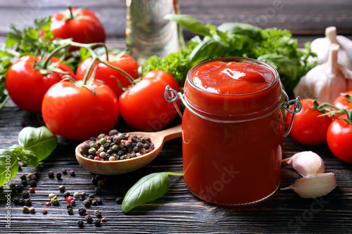 Fotografía Composition of ketchup in jar and ingredients on wooden background, closeup
