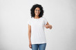 © wayhome.studio  - T-shirt design and advertising concept. Style and fashion. Indoor shot of cheerful smiling young African American woman with curly hair pointing index finger at copy space on her blank white top