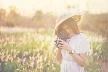 summer lifestyle portrait of pretty young woman having fun in the garden. Photographer making pictures in hipster style hat and vintage camera. Photo toned style Instagrams filters.