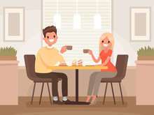 Loving Couple Is Drinking Coffee In A Cafe. A Man And A Woman Are Sitting At A Table In A Cozy Restaurant