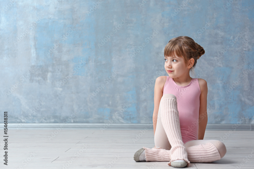 Cute little ballerina sitting on floor in dance studio