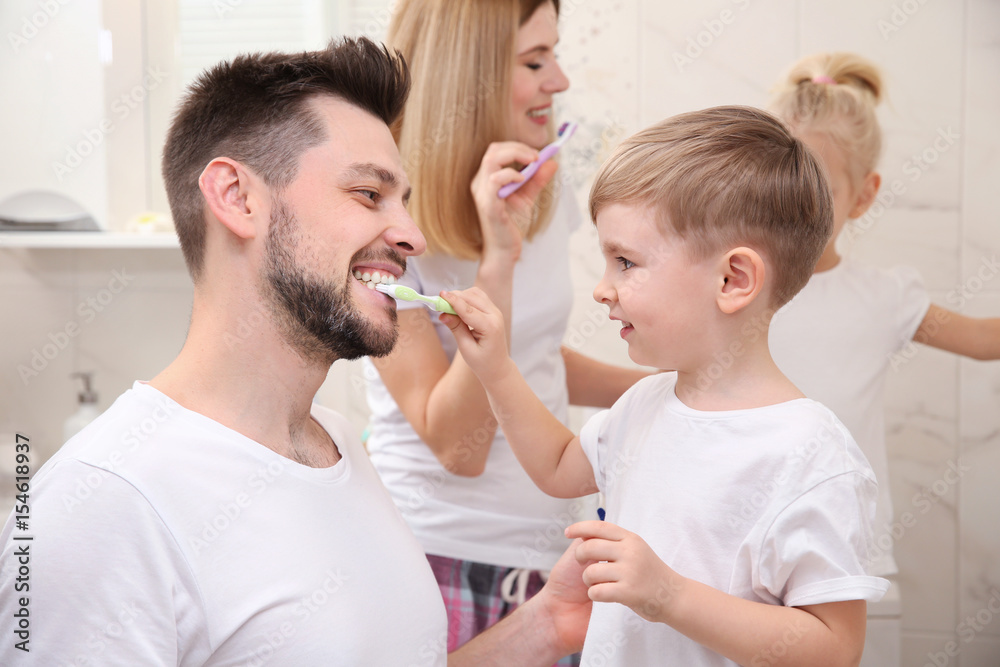 Cute little boy helping his father to brush teeth in bathroom