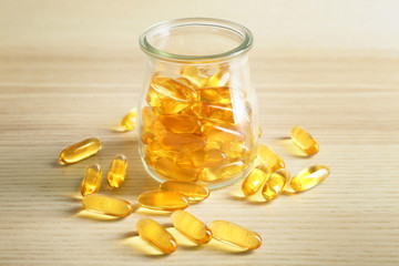 Wall Mural - Glass bottle with fish oil capsules on light wooden background