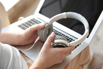 Audio book concept. Young woman using laptop with headphones, close up