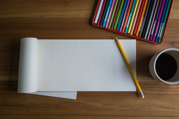 Wall Mural - open blank graph pad with pencil, color pencils and a cup of coffee on a wooden desk. empty space fo