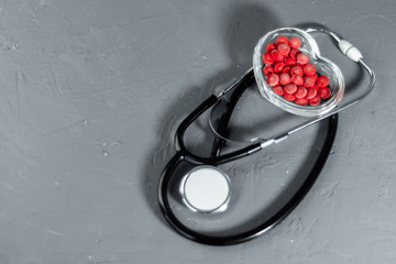 Poster - Stethoscope on a dark background with heart shaped pills