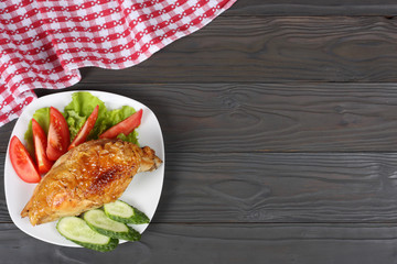 grilled chicken fillet on white plate with tomato on dark wooden background with red cloth.  With copy space. Top view.