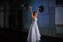 Beautiful And Muscular Bride Blonde In A Wedding Dress Doing An Exercise With A Barbell In A Gym, Crossfit