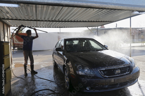 A Car Wash Worker Sprays Water While Cleaning A Car At A Garage In