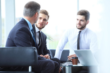 Mature businessman using digital tablet to discuss information with a younger colleague in a modern business lounge