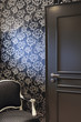 © Myriam Ramel - Resting corner with gray door with black wallpaper and golden flowers and gray armchair