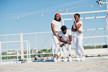 Three stylish african american friends, wear on white clothes at pier on beach. Street fashion of young black people. Black man with two african girls.