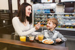 © aemstock - A young mother is feeding her little son with a spoon at a table in a cafe