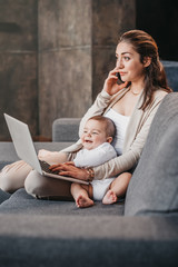 young mother working from home, talking on smartphone while spending time with her baby boy