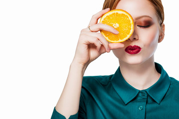 Beautiful redhead girl with professional makeup red lips with closed eyes in a green shirt with orange covers on the hand, lips, kiss, close-up white background