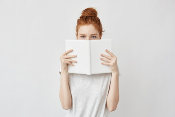 Poster - Redhead girl hiding face behind notebook looking at camera frightenedly.