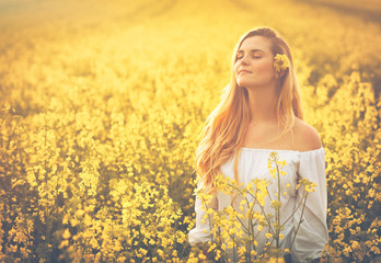 Wall Mural - Smiling woman in yellow rapeseed field at sunset