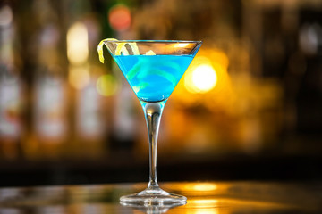 Closeup glass of blue lagoon cocktail decorated with lime at festive bar counter background.