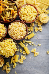 Different kinds of pasta in bowls on grey table