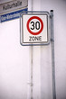 © ginton - Verkehrsschilder an Hausecke / An einer Hausecke sind ein Straßenschild und ein Hinweisschild angebracht vor denen ein Geschwindigkeitsbegrenzungsschild steht.