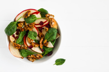 Wall Mural - Fruit salad with fresh apples, dried cranberries, spinach and walnuts in a white bowl on the wooden table, top view.