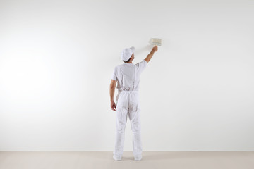 Wall Mural - Rear view of painter man looking and painting blank wall, with paint brush, isolated on white big space