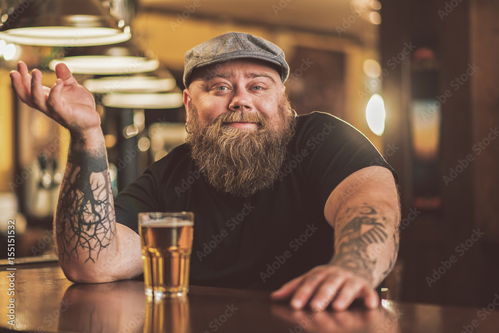 Smiling bearded male drinking beer in pub - obrazy, fototapety, plakaty 
